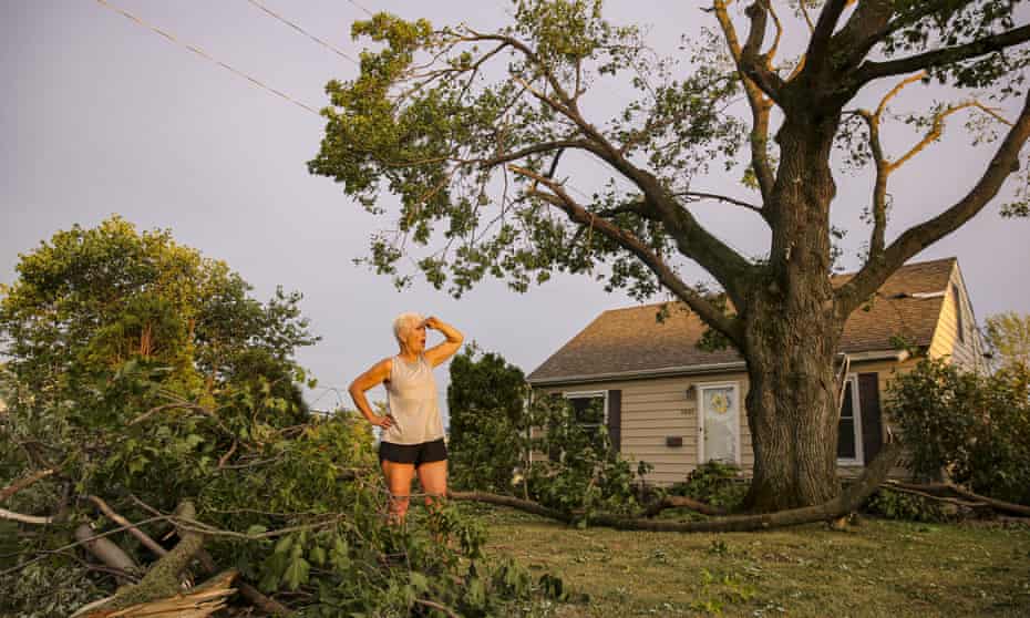 A woman stands in her front yard in Cedar Rapids, Iowa, after the storm, which blew over trees, flipped vehicle, and left thousands without power. 