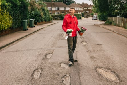 Pothole campaigner Harry Smith-Haggett, standing in a road full of potholes, holding plants in his hands