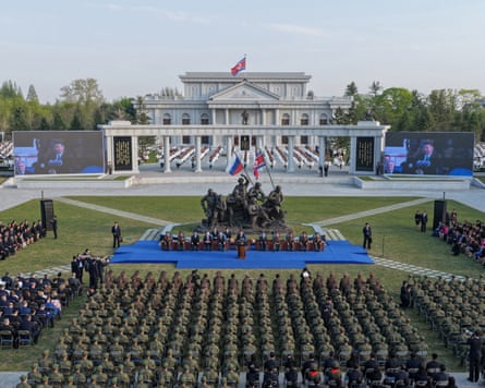 Wider shot of the ceremony with troops sitting in rows facing Kim and the statue