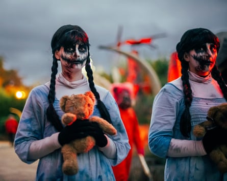 Two women dressed as scary twins with black and white face paint and black pigtails stand and stare.