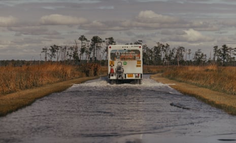 A water delivery truck drives through a flooded road in Cambridge, Maryland near Hoopers Island. “Ghost” pines, dead from salt water intrusion, are seen in the background.