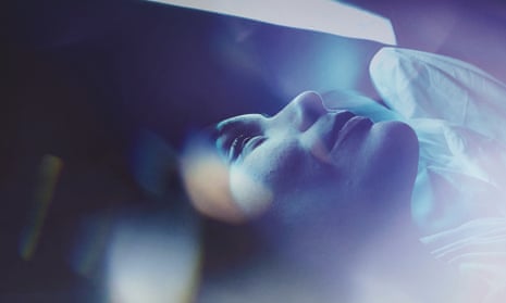 A woman slowly waking up in a bed bathed in blue light