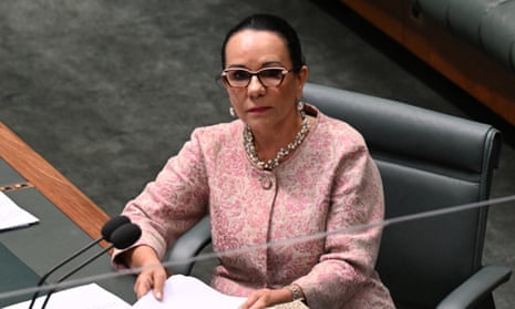 Woman wearing a pink top sits in green-coloured Parliament in Canberra