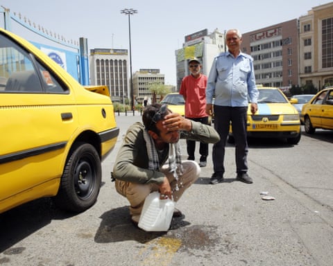 A taxi driver crouches with a water bottle splashing his face as other drivers watch on.