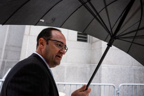 a balding man in glasses and a suit holds a large, dark umbrella