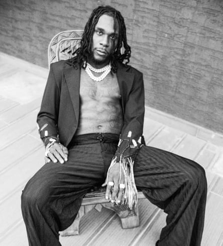 A black-and-white photograph of Burna Boy wearing a suit but no shirt