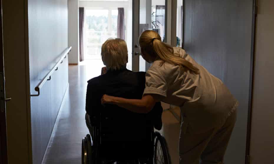 Rear view of female aged care worker with senior man sitting in wheelchair at hospital corridor