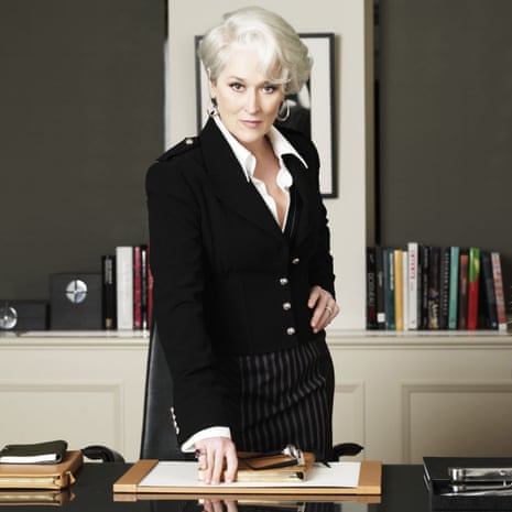 Meryl Streep, one hand on her hip and the other on a desk, looking severe and efficient in The Devil Wears Prada