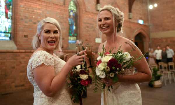 Deux femmes en robe de mariée, souriant et faisant couler des verres de champagne