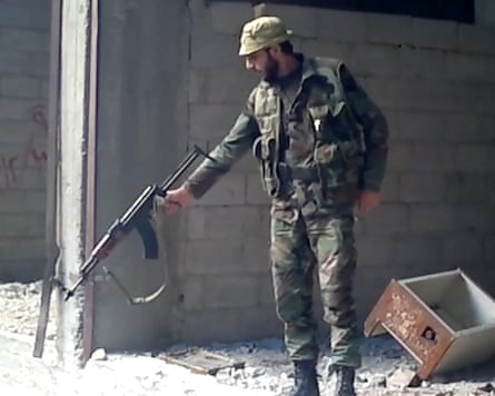 A man in combat uniform points an automatic rifle towards the ground