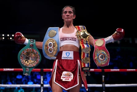 Amanda Serrano stood in the ring with several boxing title belts draped over her arms and shoulders