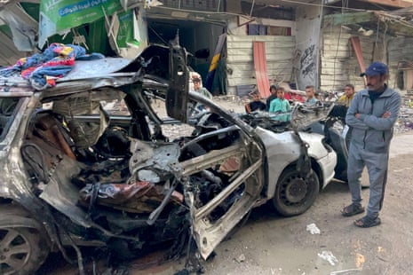 The severely damaged car containing members of Ismail Haniyeh's family is pictured, with a Palestinian man and five children looking on at the vehicle.