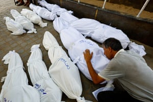 A man lays his hand on a shrouded body during the funeral for members of the Irhim family