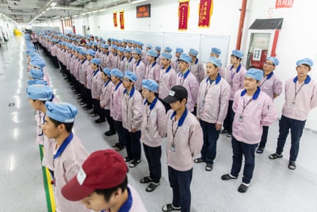 Four long lines of miserable-looking workers dressed identically