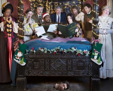 The cast of Ghosts are surrounding and sitting on a large bed, looking over at a large green book in Alison’s hands with shocked expressions.
