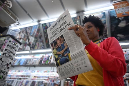 A woman holds up a newspaper reporting Lula da Silva’s election victory in a shop