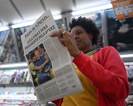 A woman holds a newspaper with an image of Lula on the front page.
