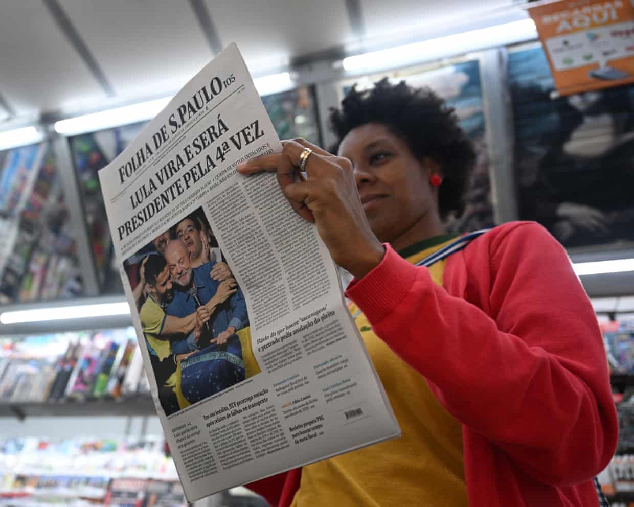 A woman holds a newspaper with an image of Lula on the front page.