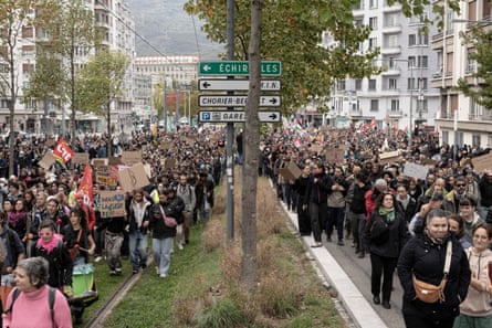 A dense crowd marches through Grenoble carrying flags and placards during a demonstration