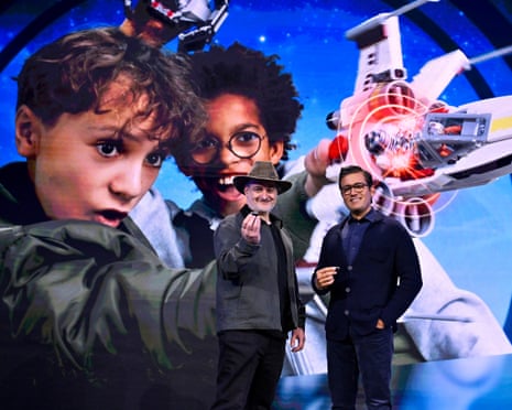 Dave Filoni and Asad Ayaz stand before an advertising backdrop for Lego's new Star Wars playsets, featuring two boys playing with Luke Skywalker's X-wing and Darth Vader's TIE fighter