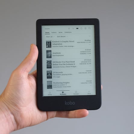 A hand holds a Kobo Clara BW e-reader in front of a grey wall