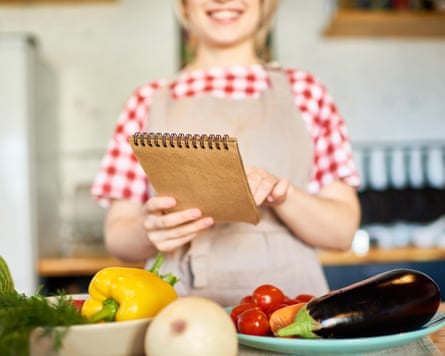 A young woman smiling and holding a notepad in front of bowls of vegetables.