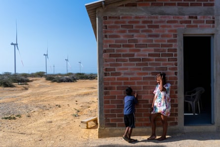 A woman laughs as she talks to a small boy outside a small brick house. A row of turbines stretch into the distance