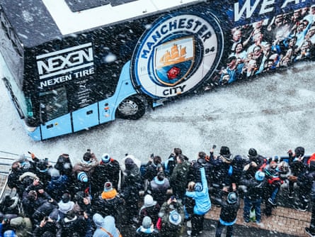 Manchester City fans look on as the team bus arrives during a snow shower prior to the match against West Ham United at the Etihad Stadium. City won the match 2-1.