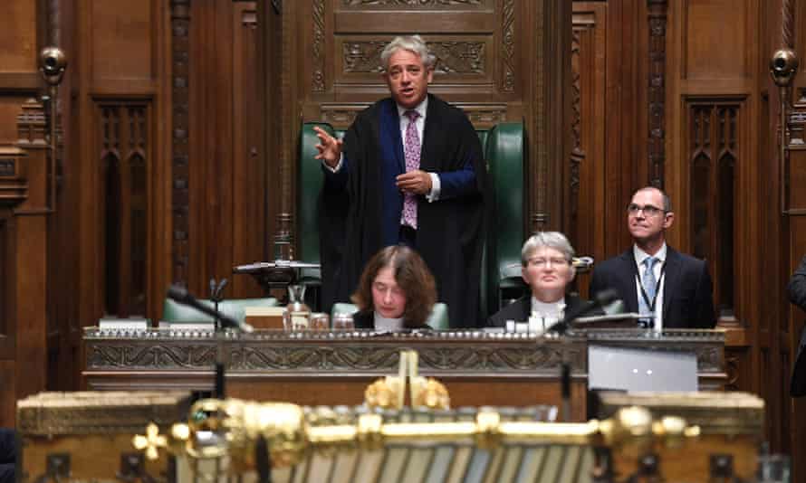 In House of Commons, gold mace in foreground out of focus, Bercow stands with three others sitting around.