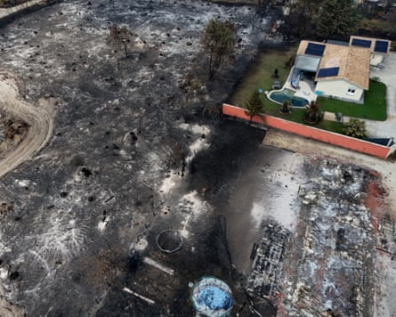 A burned and razed area of land with just one house untouched in one corner of the image