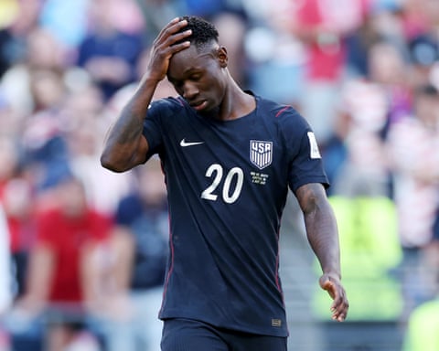 Soccer player Folarin Balogun in a dark USA jersey with number 20 holds his head, looking down