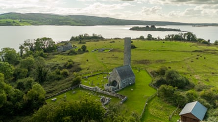 A small church, a round tower and other ruins in green fields on an island in a lake