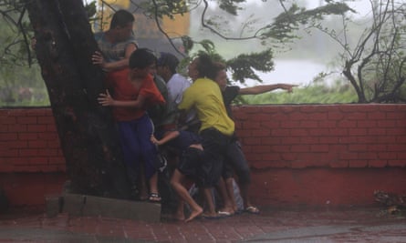 People take cover under a tree after strong winds brought by typhoon Rammasun, locally called Glenda, battered Manila, the Philippines, in July 2014.