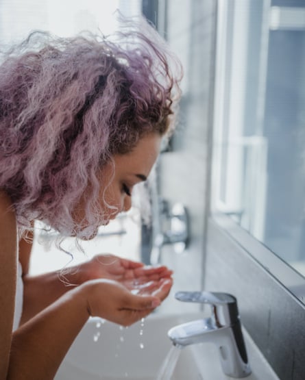 Young woman washing her face over a sink with a running tap. 