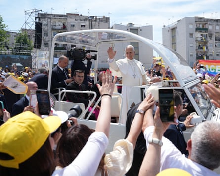 Pope stands in popemobile with crowds around.