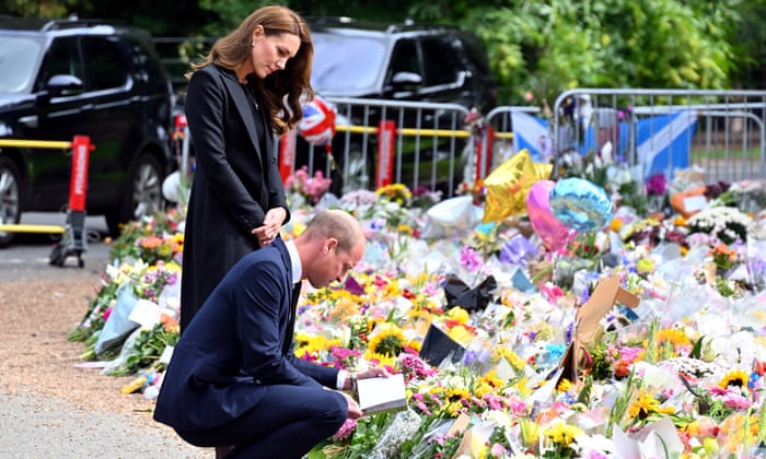 The Prince of Wales crouches while reading a card left with floral tributes to the Queen. The Prince of Wales stands, reading the card over his shoulder.