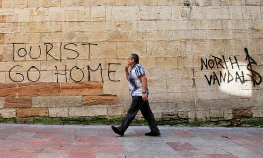 مردی از کنار دیوارنویسی «Tourists Go Home» روی دیوار نزدیک به تالار شهر در اوییدو ، شمال اسپانیا عبور می کند.