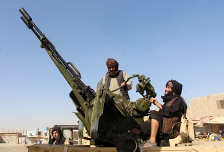 Bearded Taliban fighters wearing headdresses sit and stand around an anti-aircraft gun which points into the blue sky.