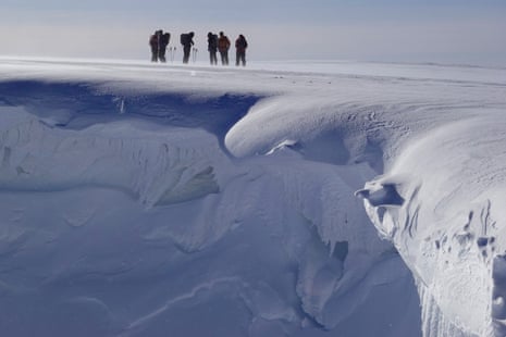 Six skiers stand close to a cornice