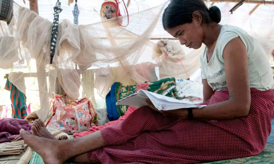 A young woman sits in an improvised tent writing in an exercise book