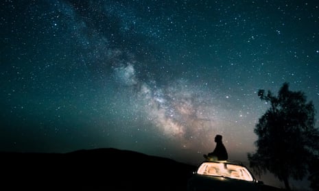 Person sitting on a car looking at stars