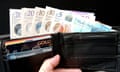 Banknotes and bank cards held up in a black leather wallet