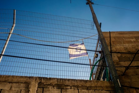 An Israeli flag flies over a house behind metal fencing