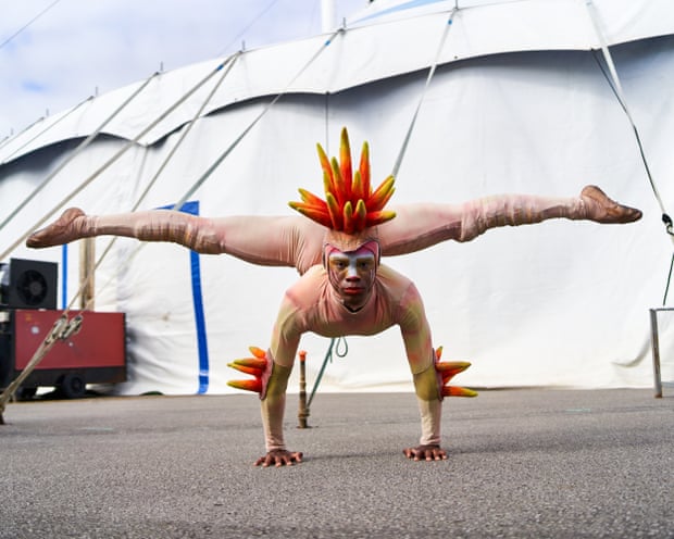 A circus contortionist in a colourful costume practicing his act by balancing with his hands on the ground and his legs stretched in the air.