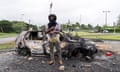 A man stands in front a burnt car during unrest in Noumea. New Caledonia has faced days of deadly violence.