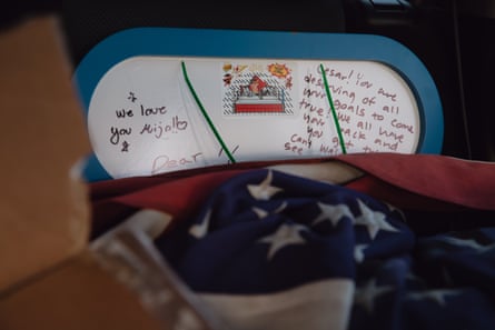 In the back seat of a car, a whiteboard filled with encouraging messages in English and Spanish sits alongside an american flag