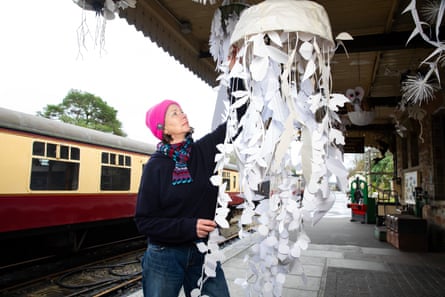 Nicola Bealing hangs a large mobile-style art work on the platform of a train station