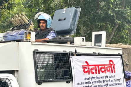 A police officer stands in an armoured vehicle with a banner warning citizens against unlawful gathering