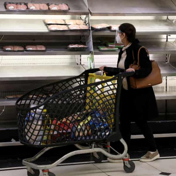 A woman pushes a shopping trolley past near-empty shelves at a supermarket