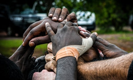 The Tiwi Bombers huddle during the quarter-time break against the Crocs. The white hand of Ashton Hams pokes into the pile, front left